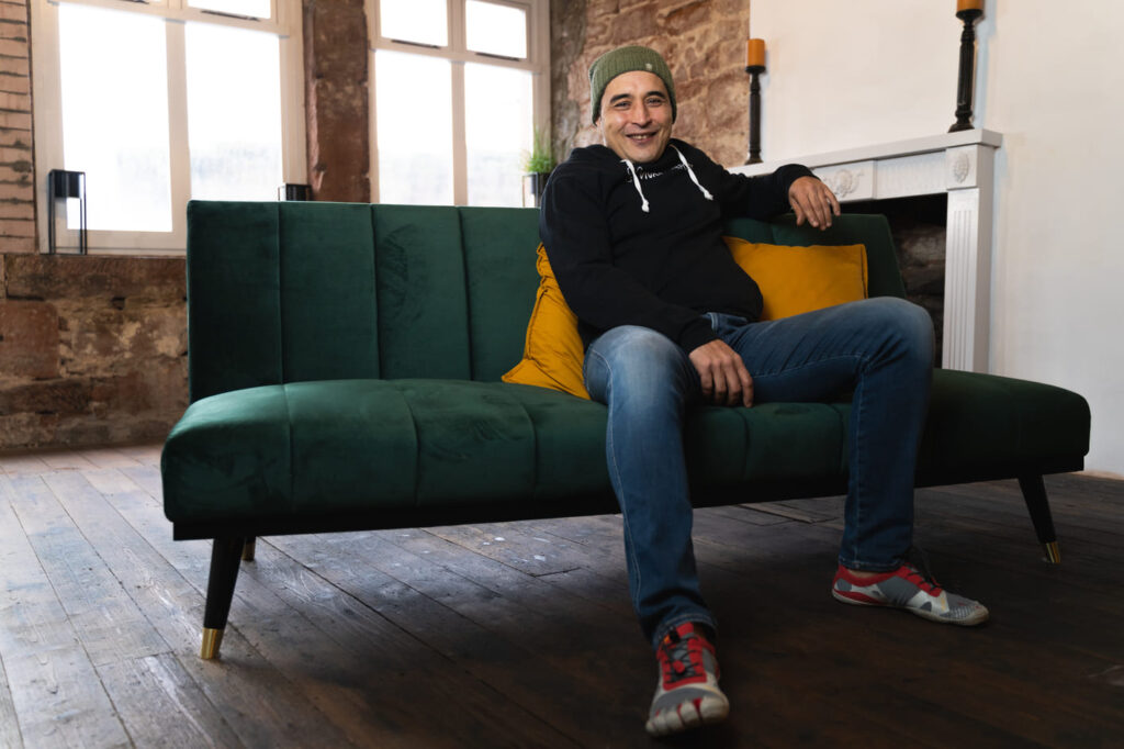 Phil Young of Your Peak Potential sitting on a green sofa smiling at camera